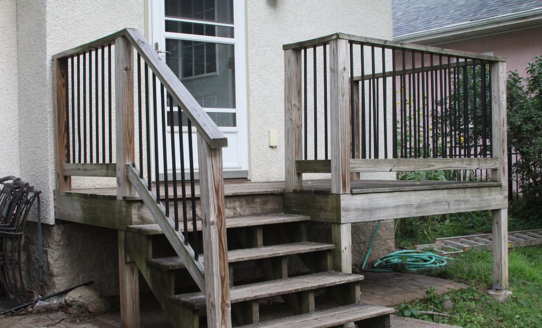 A deck with silvered grey boards, dull railings and worn stair treads, before restoration