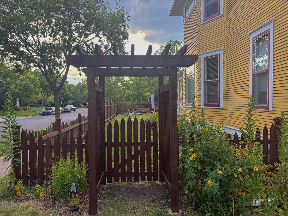The same picket fence and arbor after cleaning and staining, finished in a deep brown