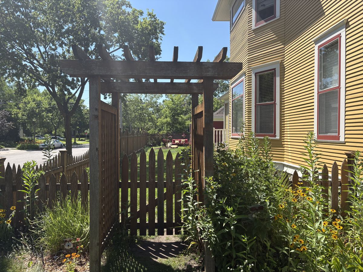 A picket fence and cedar arbor gone dry and faded, before restoration